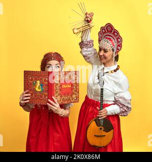 Musikerinnen in russischen Volkskleidern mit Musikinstrumenten auf gelbem Studiohintergrund - Moskau, Russland, 17. Juni 2022 Stockfoto