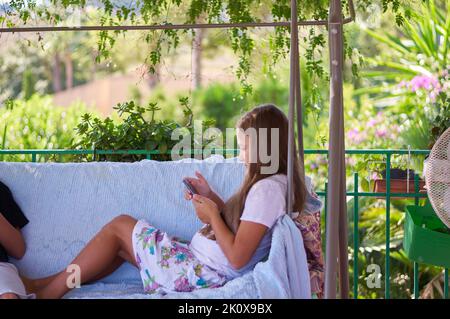 Jungen Mädchen auf der Terrasse mit Geräten sitzen Stockfoto