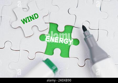 Ökologisches Konzept. Weiße Puzzles liegen auf einem grünen Hintergrund, anstelle eines offenen Puzzles steht geschrieben -Wind Energy Stockfoto