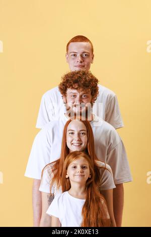 Fröhliche, rothaarige Jugendliche, lächelnde Jungen und Mädchen, die die Kamera auf gelbem Hintergrund betrachten. Lustige Treppe. Diversity-Konzept Stockfoto