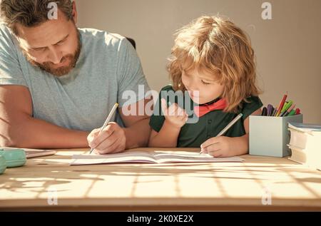 Bärtiger Vater schreibt Schulaufgaben mit seinem Sohn im Klassenzimmer, zurück zur Schule Stockfoto