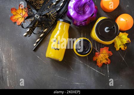 Halloween-Mocktails. Kürbiscocktails und Limonade in Gläsern mit gruseligen Gesichtern und Dekoration auf dunklem Steingrund. Blick von oben Stockfoto