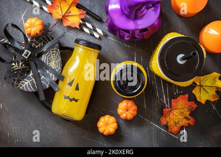 Halloween-Mocktails. Kürbiscocktails und Limonade in Gläsern mit gruseligen Gesichtern und Dekoration auf dunklem Steingrund. Blick von oben Stockfoto