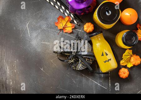 Halloween-Mocktails. Kürbiscocktails und Limonade in Gläsern mit gruseligen Gesichtern und Dekoration auf dunklem Steingrund. Blick von oben Stockfoto