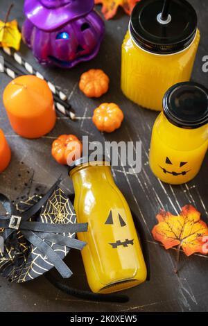 Halloween-Mocktails. Kürbiscocktails und Limonade in Gläsern mit gruseligen Gesichtern und Dekoration auf dunklem Steingrund. Stockfoto