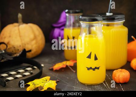 Halloween-Mocktails. Kürbiscocktails und Limonade in Gläsern mit gruseligen Gesichtern und Dekoration auf dunklem Steingrund. Stockfoto