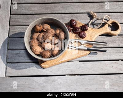 Walnüsse in einer Schüssel und Kastanien auf einem Holzbrett mit einem Nussknacker und einem Holztisch Stockfoto