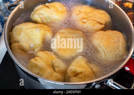 Kochender Knödel im großen Topf. Süße Fruchtknödel, die in kochendem Wasser in einem Topf auf einem Keramikkochfeld schwimmen, Nahaufnahme. Zubereitung von Speisen. Stockfoto