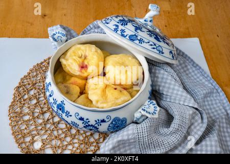 Gekochte süße Pflaumenknödel in offener dekorativer Schüssel mit Deckel, Handtuch, Bambuskissen auf dem Tisch, Nahaufnahme. Stockfoto