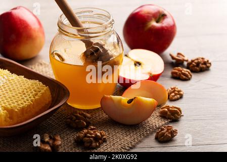 Einmachglas mit Honig, Honigtaube, Honigwabe, roten Äpfeln und Walnüssen auf Küchentisch Stockfoto