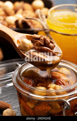 Honigwurz verschiedene Nüsse in Holzlöffel über Einmachglas Bio-Lebensmittel Hintergrund Stockfoto