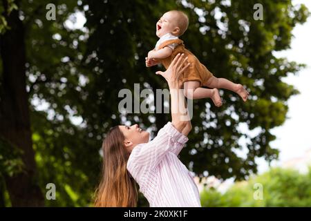 Foto von liebenswert charmante Mutter kleine Tochter tragen lässige Outfits spielen werfen Arme zu Fuß außerhalb des Gartens Stockfoto