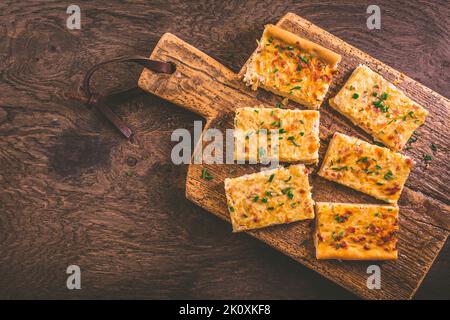 Zwiebelkuchen – hausgemachter, herzhafter deutscher Zwiebelkuchen oder Kuchen mit gedämpften Zwiebeln und Speck auf einem Holzbrett Stockfoto