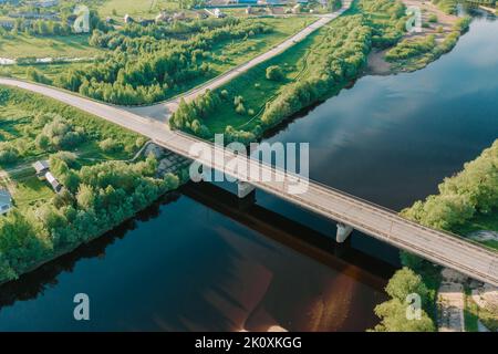 Drohnenansicht einer leeren Autobrücke über den wunderschönen blauen Fluss. Luftperspektive Brücke in der Nähe von Häusern im hellen Sommer. Abendlicht. Fantastische Drohnenaufnahme Stockfoto