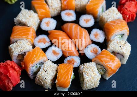 Set Sushi-Rolle mit Lachs, Avocado, Frischkäse, Gurke, Reis, Thunfisch auf dem schwarzen Teller Stockfoto