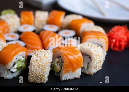 Sushi auf dem Teller, Mittagessen im Restaurant. Set Sushi-Rolle mit Lachs, Avocado, Frischkäse, Gurke, Reis, Thunfisch auf dem schwarzen Teller Stockfoto