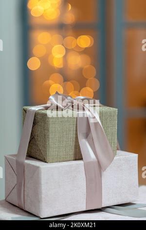 Nahaufnahme von festlich verpackten Geschenkschachteln, auf einem weihnachtlichen Hintergrund mit funkelnden Lichtern, einem magischen Neujahrshintergrund. Unschärfe-Effekt, weicher selektiver Fokus Stockfoto