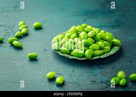 Schüssel mit rohen Edamamabohnen auf cyanfarbenem Hintergrund Stockfoto