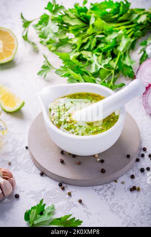 Chimichurri - hausgemachte frische lateinamerikanische Sauce aus verschiedenen Kräutern, Knoblauch und Rotweinessig. Zutat zum Kochen oder Beilage auf dem Tisch Stockfoto