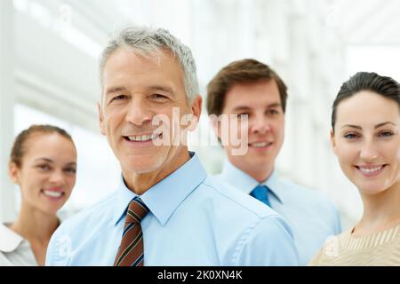 Selbstbewusster Geschäftsmann mit Kollegen im Hintergrund. Porträt eines selbstbewussten, reifen Geschäftsmanns mit Kollegen im Hintergrund. Stockfoto