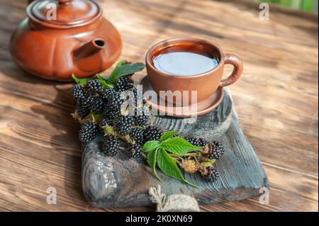 Tee mit Brombeeren. BlackBerry-Tee mit frisch gepflückten Brombeeren in einer Keramikbecher auf dem Hintergrund eines schönen Holz Schneidebrett .The con Stockfoto