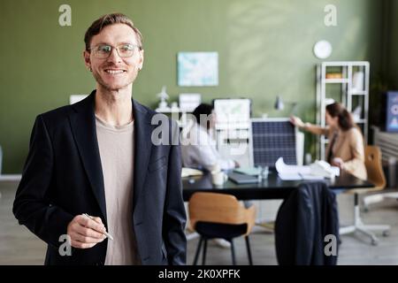 Porträt eines jungen professionellen Ingenieurs, der die Kamera lächelt, während er im Büro steht Stockfoto