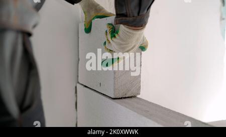 Der Baumeister verlegt eine Wand aus Gasblöcken mit Werkzeugen und Klebmörtel. Konstruktion aus ACC-Blöcken. Ein Arbeiter baut aus einer Innenwand eines Hauses Stockfoto