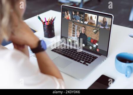 Kaukasische Geschäftsfrau am Schreibtisch, die mit verschiedenen winkenden Kollegen einen Videoanruf auf einem Laptop führt. Geschäftskommunikation, Remote-Arbeit und digitale Schnittstelle Stockfoto