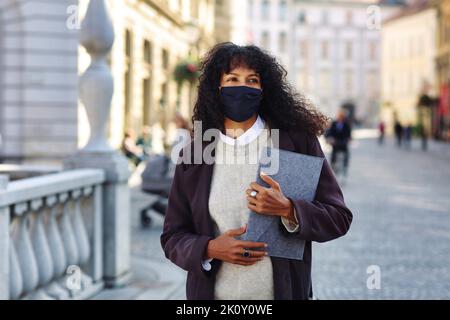 Geschäftsfrau steht auf der Straße mit Gesichtsmaske, die Ordner mit Dokumenten hält Stockfoto