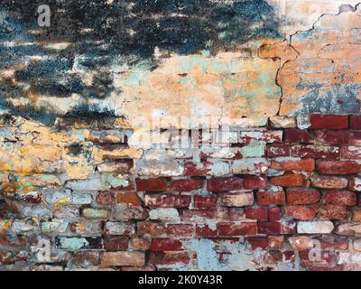 Sehr alte Ziegelwand mit Rissen und beschädigter Stuckoberfläche, abgenutzte Farbschichten, die sich ablösen. Grunge Textur und Hintergrund. Stockfoto