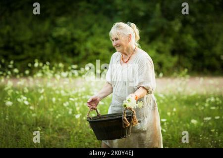 Ältere Frau in weißem Kleid hält das A-Becken mit Wasser. Stockfoto