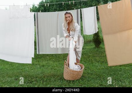 Wäschereitag. Eine Frau hängt Bettwäsche und Handtücher auf einem Baum im Hof eines Dorfhauses. Sommerhaus-Konzept. Stockfoto