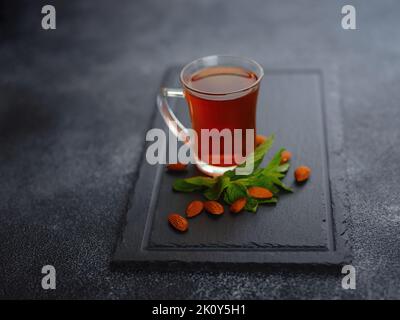 Tasse frisch gebrühten schwarzen Tee mit Minze und Mandelnüssen, warmes, weiches Licht, dunkler Hintergrund. Stockfoto