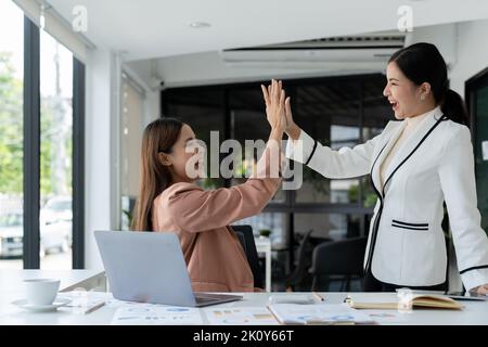 Geschäftsfrauen geben fünf Hände und Daumen nach oben während des Meetings, um geschäftliche Erfolge und Erfolge mit Teamarbeit zu feiern Stockfoto