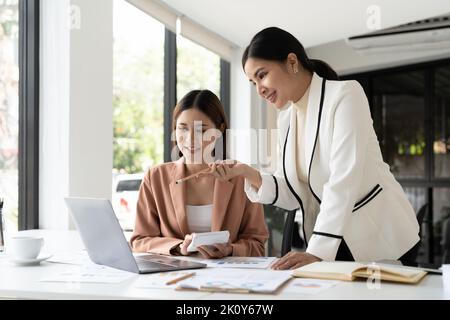 Junge Geschäftsfrau, die vor dem Laptop steht und Verkaufsmitarbeitern Ratschläge gibt. Unternehmensberatung im Büro. Stockfoto