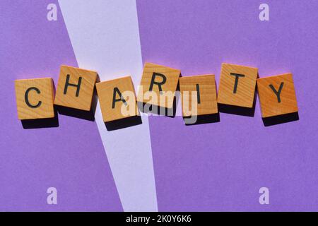 Charity, Wort in hölzernen Buchstaben auf violettem Hintergrund isoliert Stockfoto