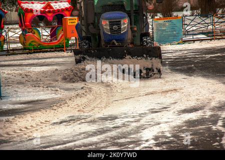 Dnipropetrovsk, Ukraine - 01.18.2022: Ein Arbeiter auf einem Traktor entfernt Schnee im Stadtpark. Stockfoto