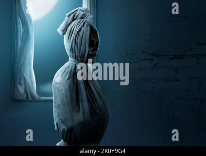 Pocong ist mit einem weißen Leinentuch bedeckt, das auf einem verlassenen Haus steht. Halloween-Konzept Stockfoto