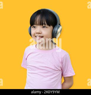 Portrait von jungen Mädchen hört Musik mit modernen Kopfhörern auf gelbem Hintergrund isoliert. Kind Mädchen genießen Rhythmen beim Hören von Musik mit h Stockfoto