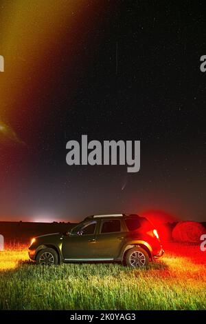 Komet Neowise C2020 F3 in der Nacht Sternenhimmel über Auto-SUV im Sommer Landwirtschaftliche Feldlandschaft. Suv In Der Nacht Sommer Wiese Landschaft Mit Hay Bale Stockfoto