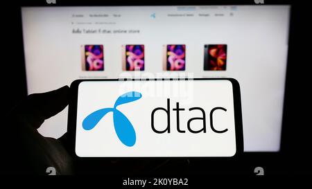 Person, die das Telefon mit dem Logo von Total Access Communication Public Company Limited (DTAC) auf dem Bildschirm vor der Webseite hält. Konzentrieren Sie sich auf die Telefonanzeige. Stockfoto