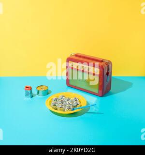 Rotes Retro-Radio, gelbe Plastikteller, glänzende Disco-Kugeln, blauer Plastiklöffel, Lebensmittelkisten aus Metall und Reibe auf gelbem und blauem Hintergrund. Stockfoto