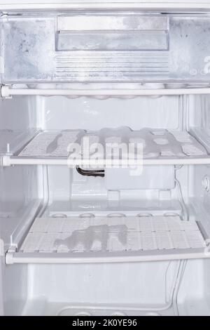 Tiefkühlschrank. Regale und Lebensmittelbehälter mit schmelzendem Eis bedeckt, Wasser im Kühlschrank. Stockfoto