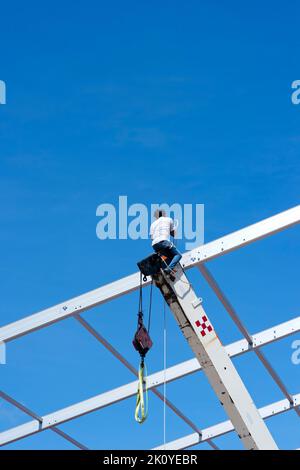 Ein Bauarbeiter, der auf dem ausgedehnten Boom eines Krans gegen den blauen Himmel in Mexiko balanciert Stockfoto