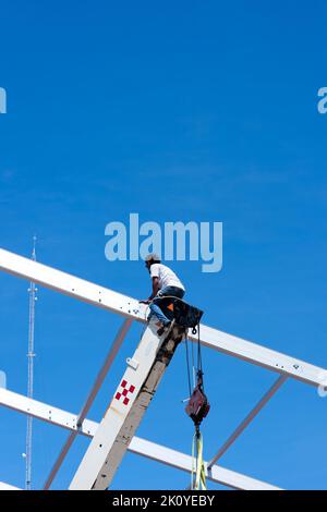 Facharbeiter, der auf dem ausgefahrenen Boom eines Krans sitzt und in Mexiko ein Dachgitter installiert Stockfoto