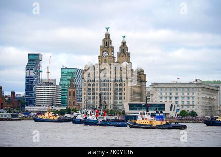 Flussschlepper führen Fleur De Lis vor, als sich Schiffe auf dem River Mersey in Liverpool vor den Three Graces (Liver Building, Cunard Building und Port of Liverpool Building) für eine maritime Hommage an Königin Elizabeth II. Versammeln. Die vor ihrer Beerdigung am Montag in der Westminster Hall in London im Staat liegen wird. Bilddatum: Mittwoch, 14. September 2022. Stockfoto