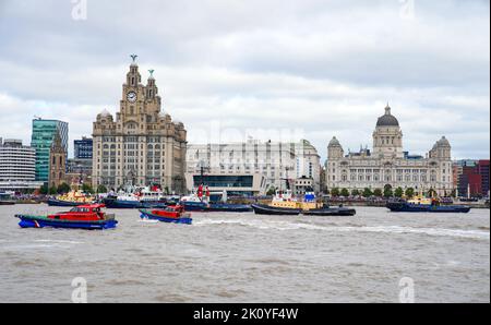 Flussschlepper führen Fleur De Lis vor, als sich Schiffe auf dem River Mersey in Liverpool vor den Three Graces (Liver Building, Cunard Building und Port of Liverpool Building) für eine maritime Hommage an Königin Elizabeth II. Versammeln. Die vor ihrer Beerdigung am Montag in der Westminster Hall in London im Staat liegen wird. Bilddatum: Mittwoch, 14. September 2022. Stockfoto