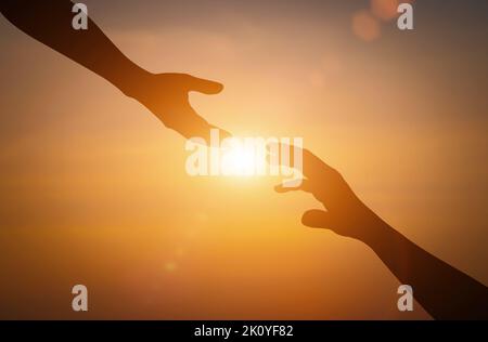 Silhouette des Erreichens, eine helfende Hand geben, hoffen und unterstützen einander über Sonnenuntergang Hintergrund. Stockfoto