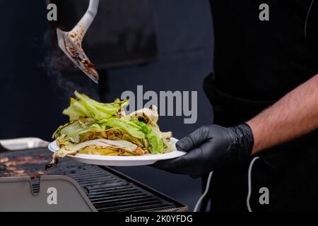 Koch hält Teller mit gegrillten Kohlblättern - Kochen im Freien Stockfoto