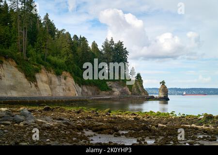 Siwash Rock Seawall Shoreline Vancouver. Siwash Rock und der felsige Strand auf der Westseite des Stanley Parks mit Frachtern in English Bay. Vancouver, B Stockfoto